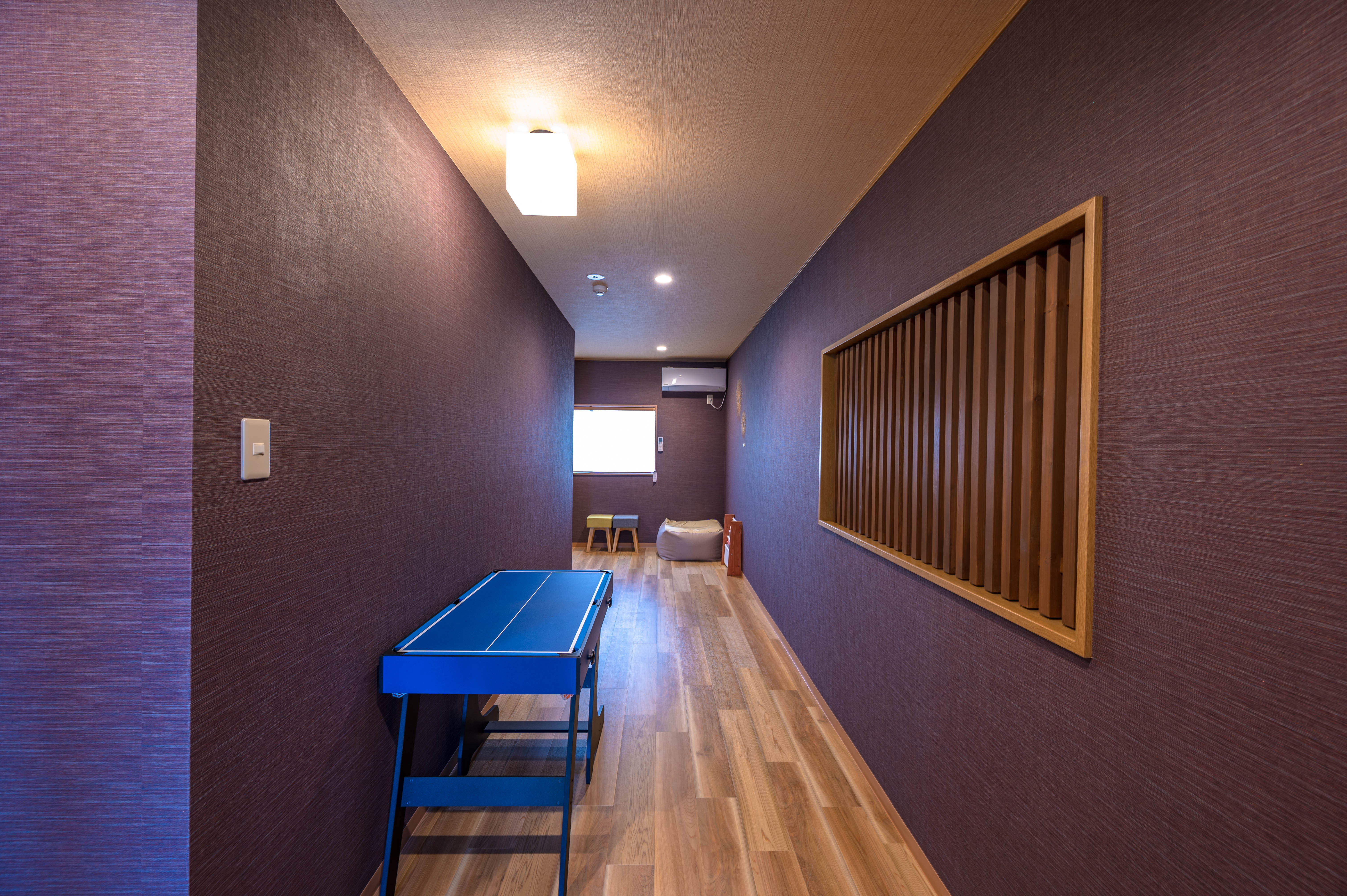 2F game room with burgundy walls, blue ping pong table, wooden slatted wall panel, and bean bag seating
