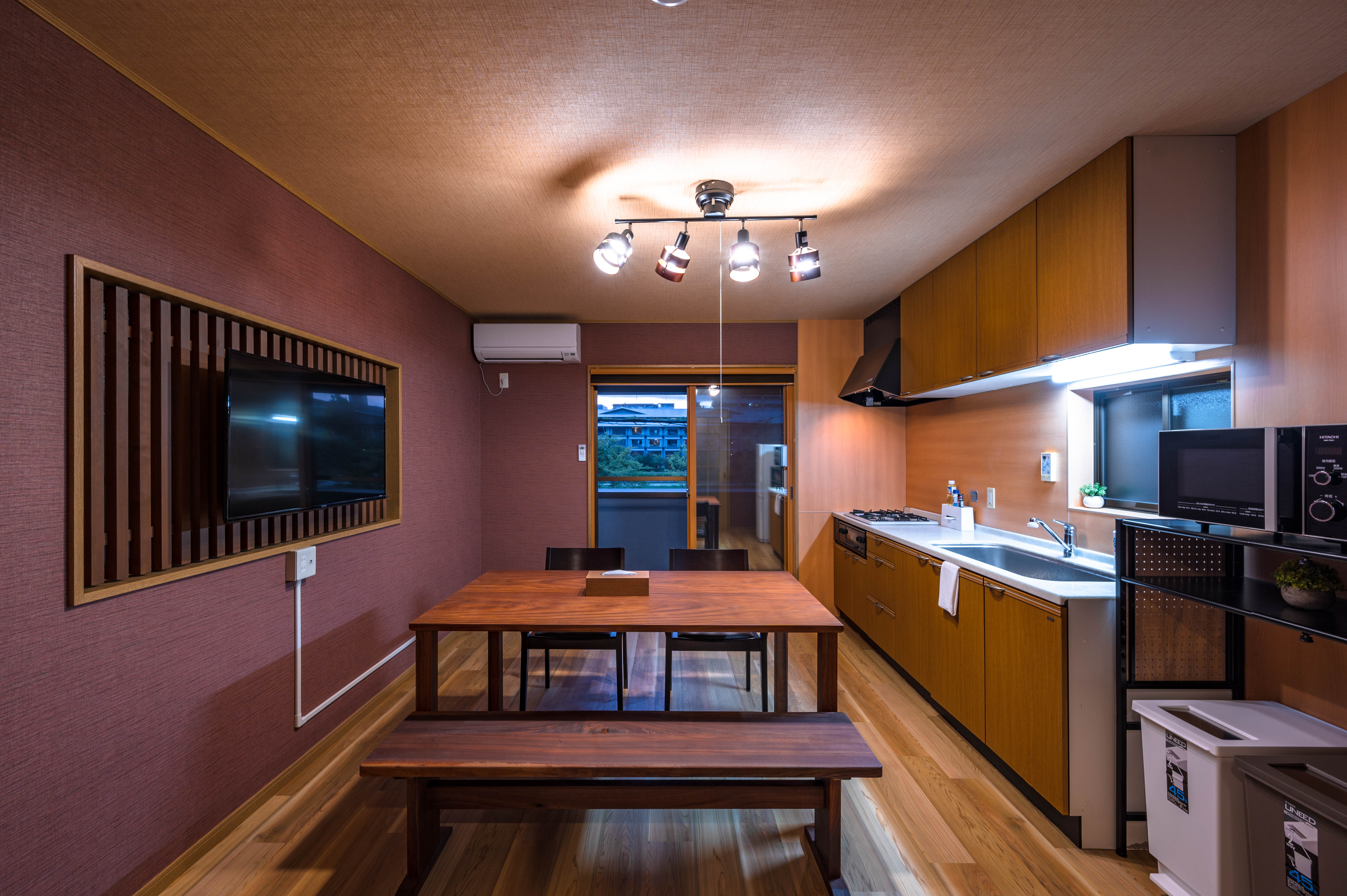 2F kitchen and dining room with burgundy walls, wooden dining table with bench seating, TV with slatted frame, and full kitchen