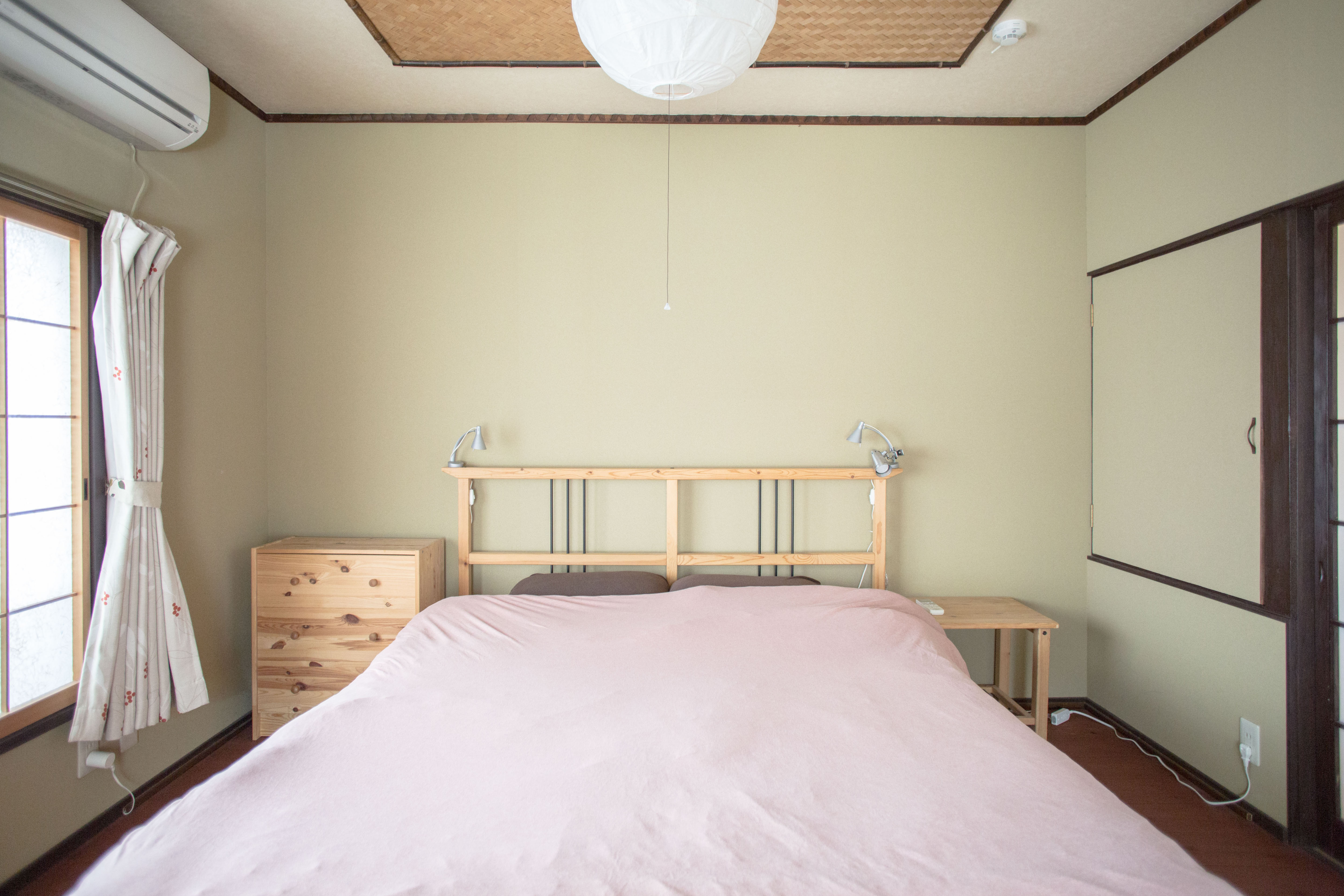 Western-style bedroom with double bed, sage green walls, bamboo ceiling accent, and pine wood furniture