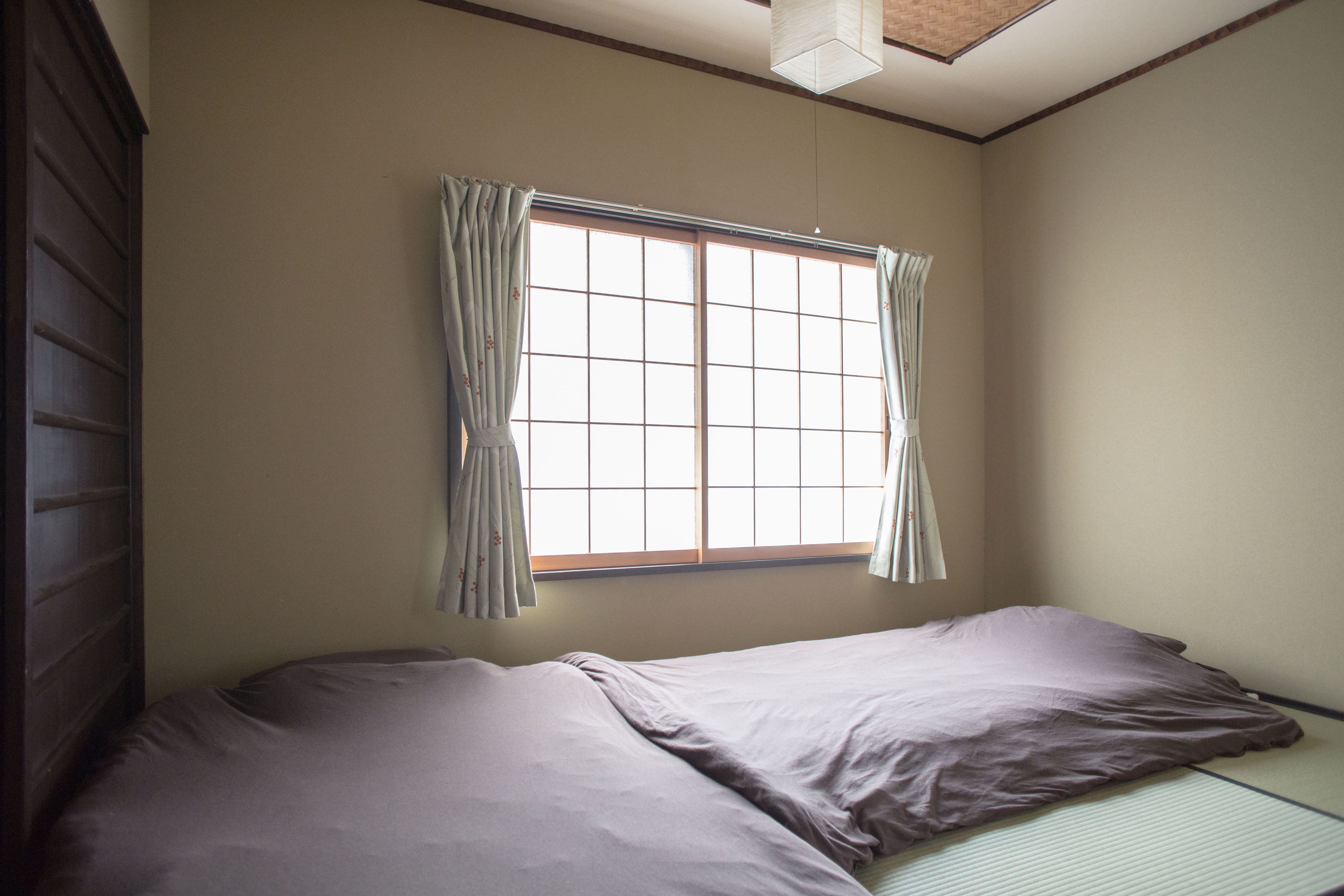 Japanese tatami room with two gray futons, shoji window with sage curtains, and woven bamboo ceiling accent