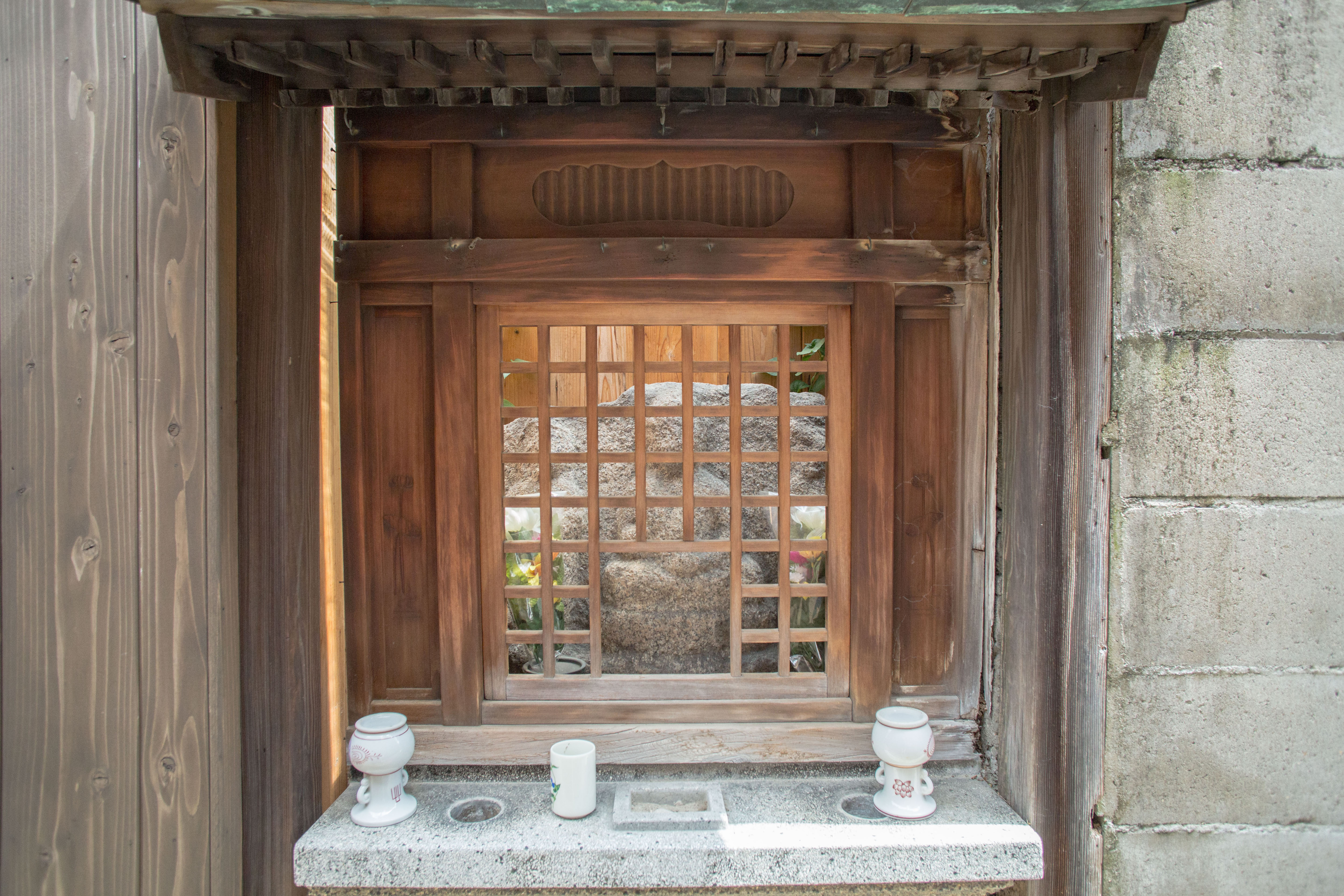 Traditional hokora shrine with wooden lattice door protecting a stone Jizo statue